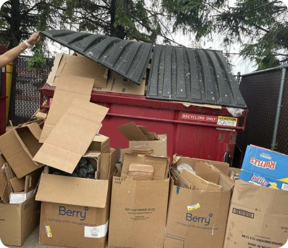 Overflowing red dumpster surrounded by cardboard boxes