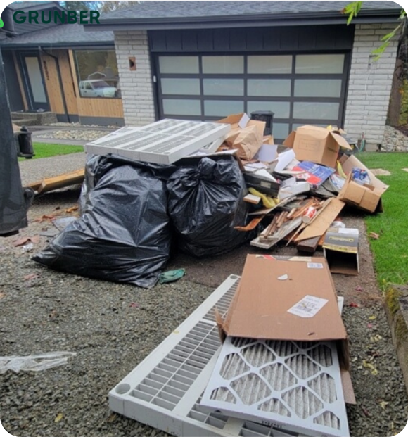 Construction debris including black bags and cardboard piled in front of a garage